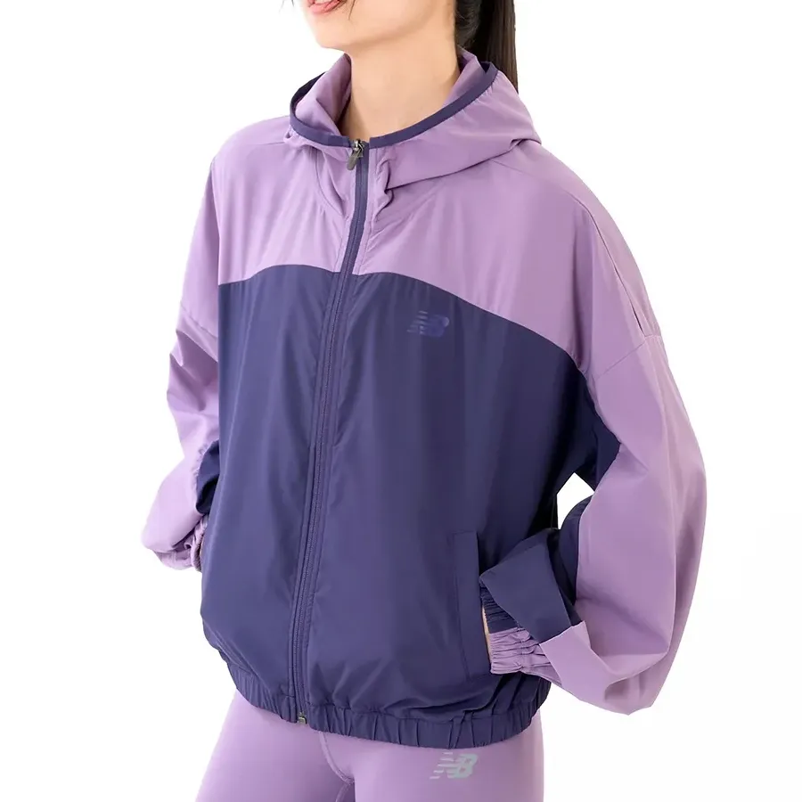 Jaqueta feminina New Balance Sport Woven roxa com capuz e zíper frontal, design esportivo com detalhes em azul escuro.